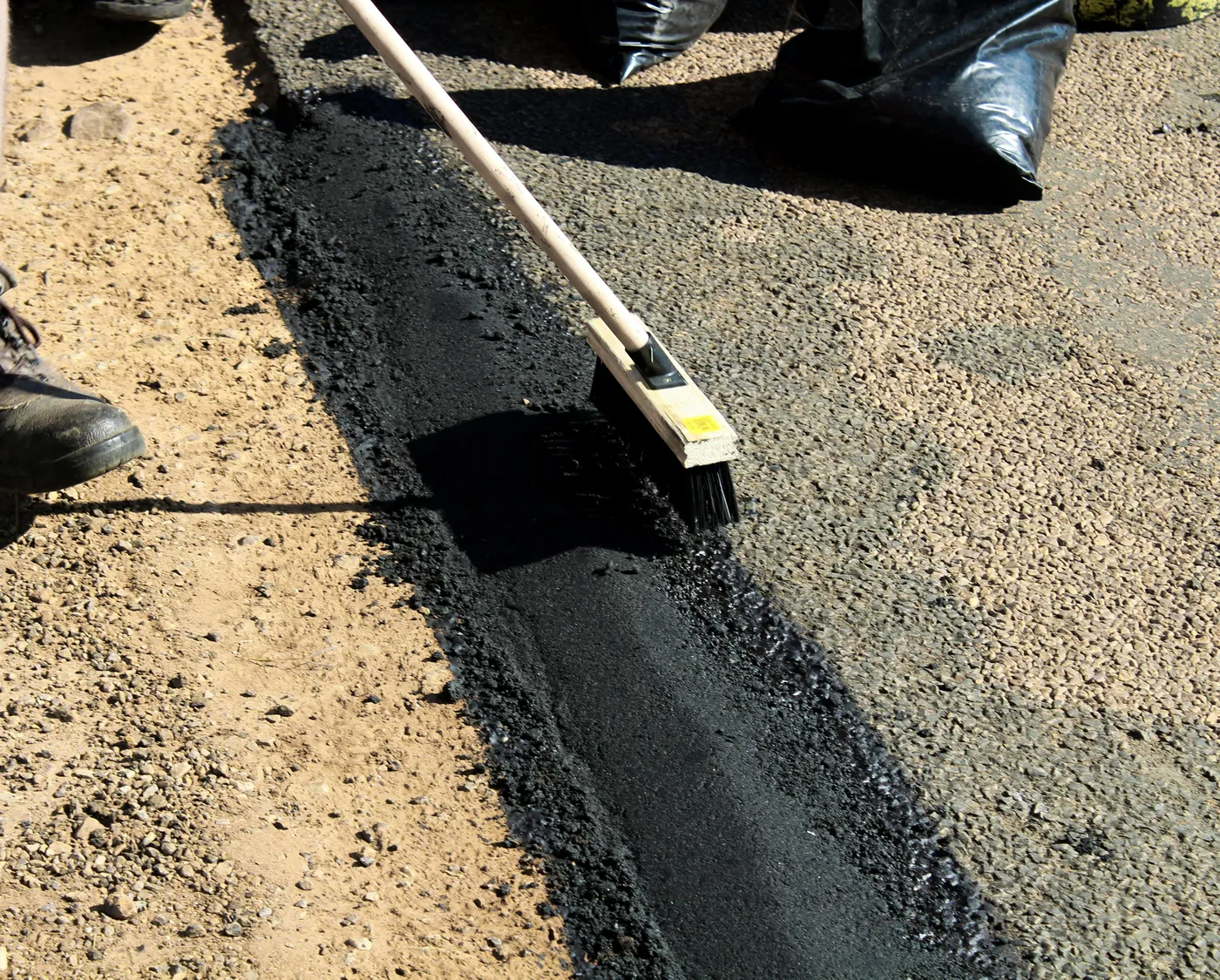 A Virginia Asphalt Services Inc. crew member hand-brooming the edge of a fresh asphalt mat against a gravel shoulder