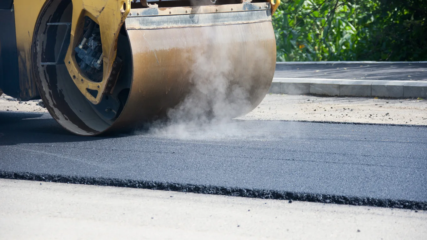A roller compacting a fresh asphalt mat against a concrete edge